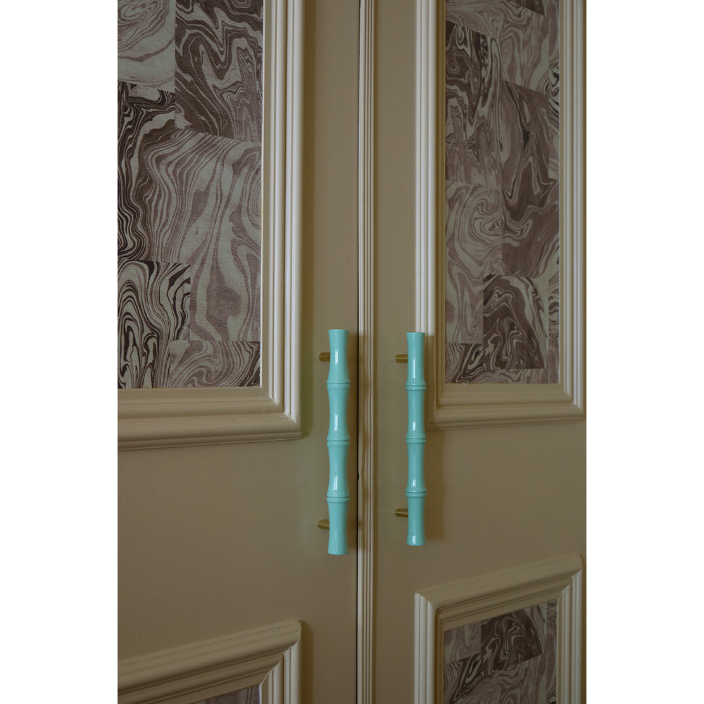 Soft butter yellow cabinet door with decorative wallpapered panels and turquoise handles on a white background