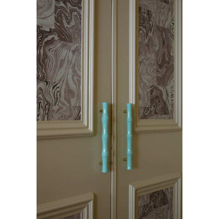 Soft butter yellow cabinet door with decorative wallpapered panels and turquoise handles on a white background