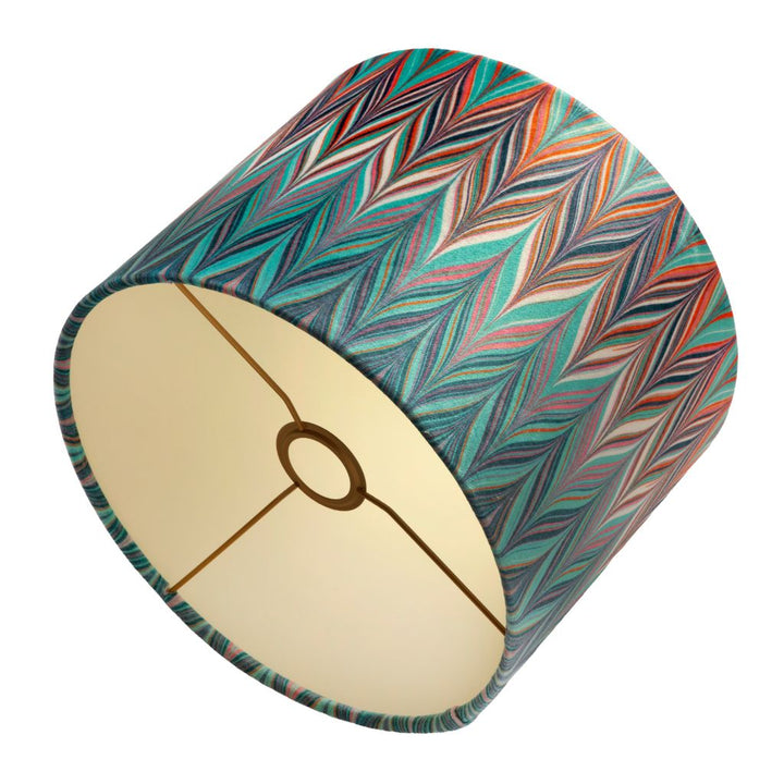 A drum velvet lampshade with a colourful chevron pattern in teal, orange, red, and navy, featuring a coloured interior.
