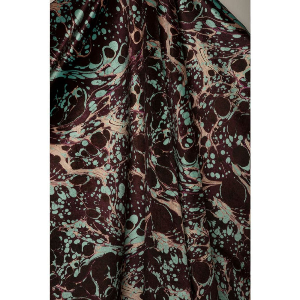 A close-up of draped fabric with an abstract marbled pattern in deep brown, mint green, and pale blush pink.