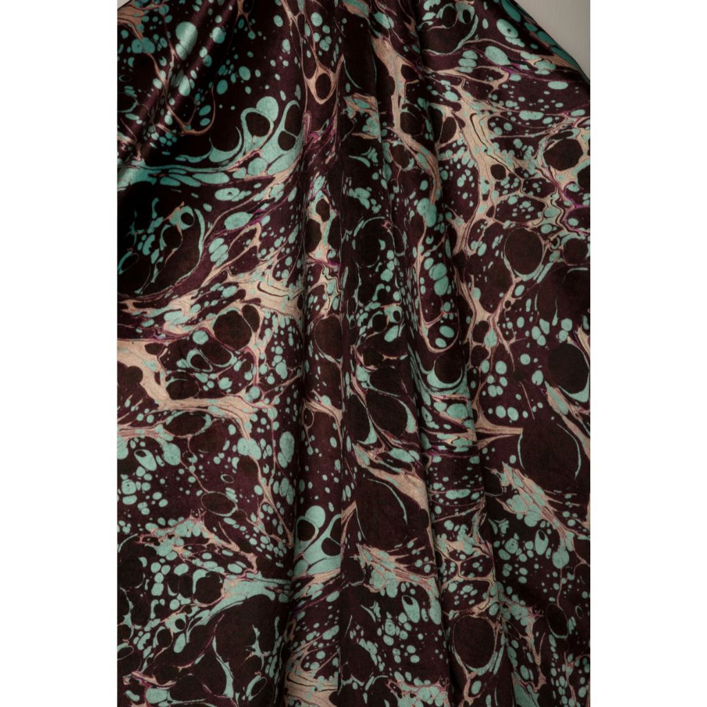 A close-up of draped fabric with an abstract marbled pattern in deep brown, mint green, and pale blush pink.