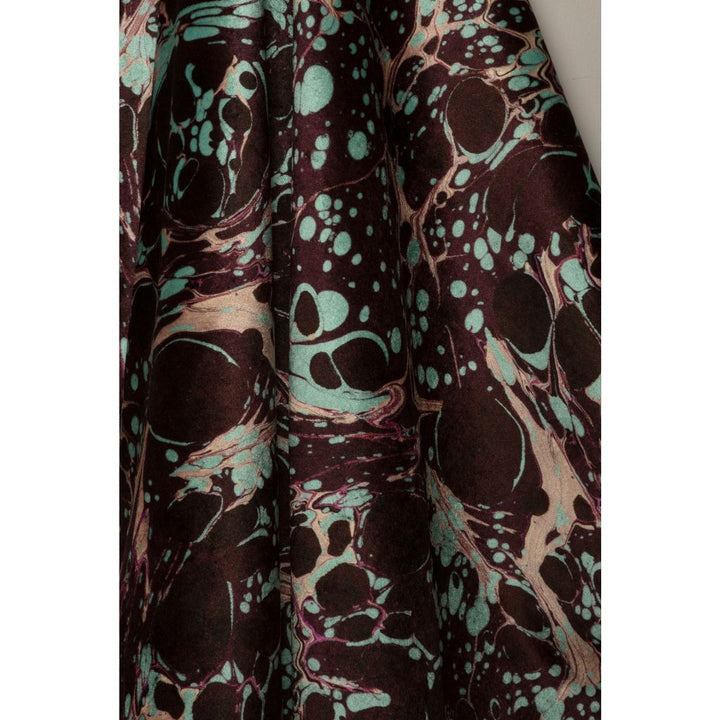 A close-up of draped fabric with an abstract marbled pattern in deep burgundy, black, and mint green.