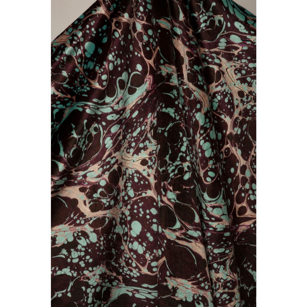 A close-up of draped fabric with an abstract marbled pattern in dark brown, black, teal, and beige.