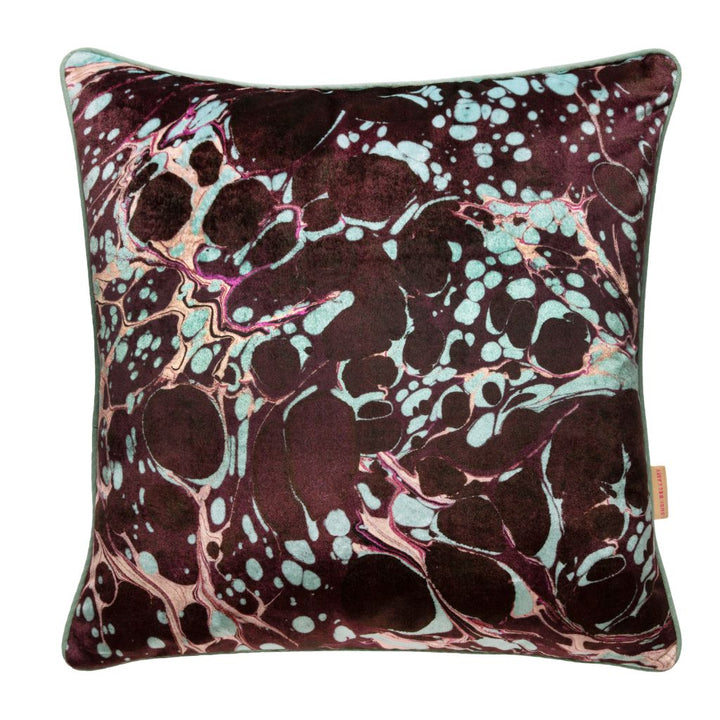 A square decorative throw pillow featuring a marbled abstract pattern in deep burgundy, light aqua, and metallic pink, with a thin light green piped edge and a small tan brand tag on the right side.