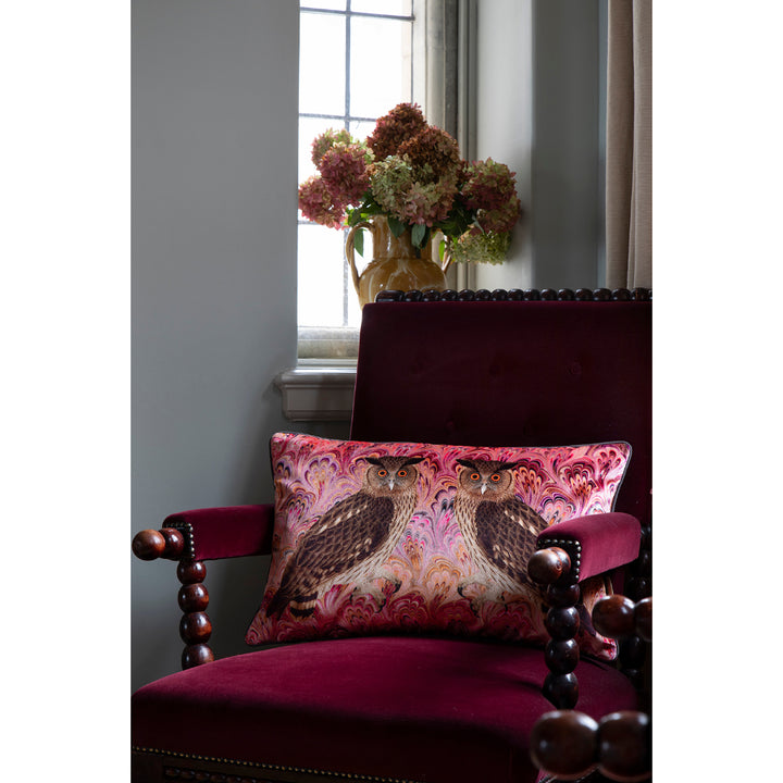 Decorative cushion with owl design on a plush chair next to a window with flowers