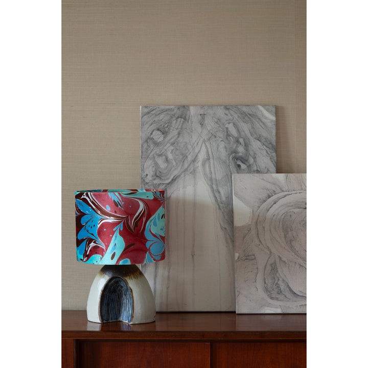 A drum lampshade featuring a marbled pattern of red, teal, brown, and white, on a midcentury sideboard with minimal art behind