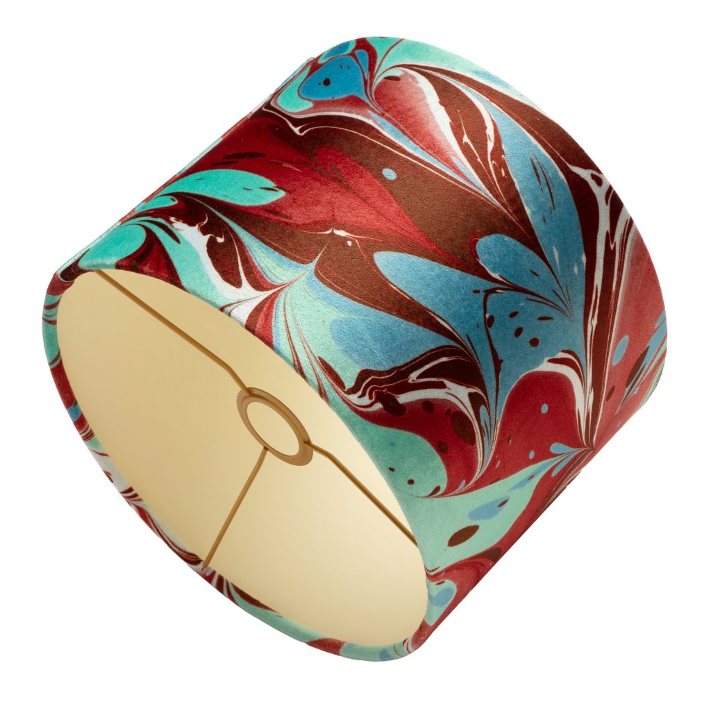 A drum lampshade featuring a marbled pattern of red, teal, brown, and white, with a cream-colored fabric interior