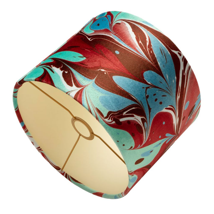 A drum lampshade featuring a marbled pattern of red, teal, brown, and white, with a cream-colored fabric interior