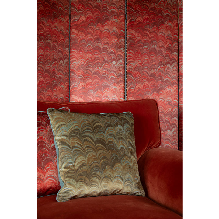 Red sofa with a pale blue and mustard patterned pillow against a red marbled wall.