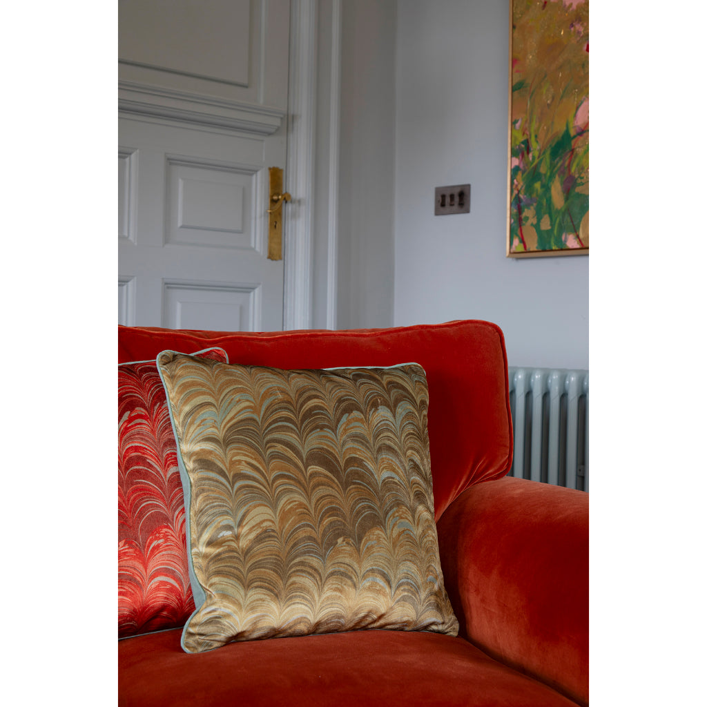 Red sofa with a pale blue and mustard patterned pillow in a room with a white door and colourful painting.