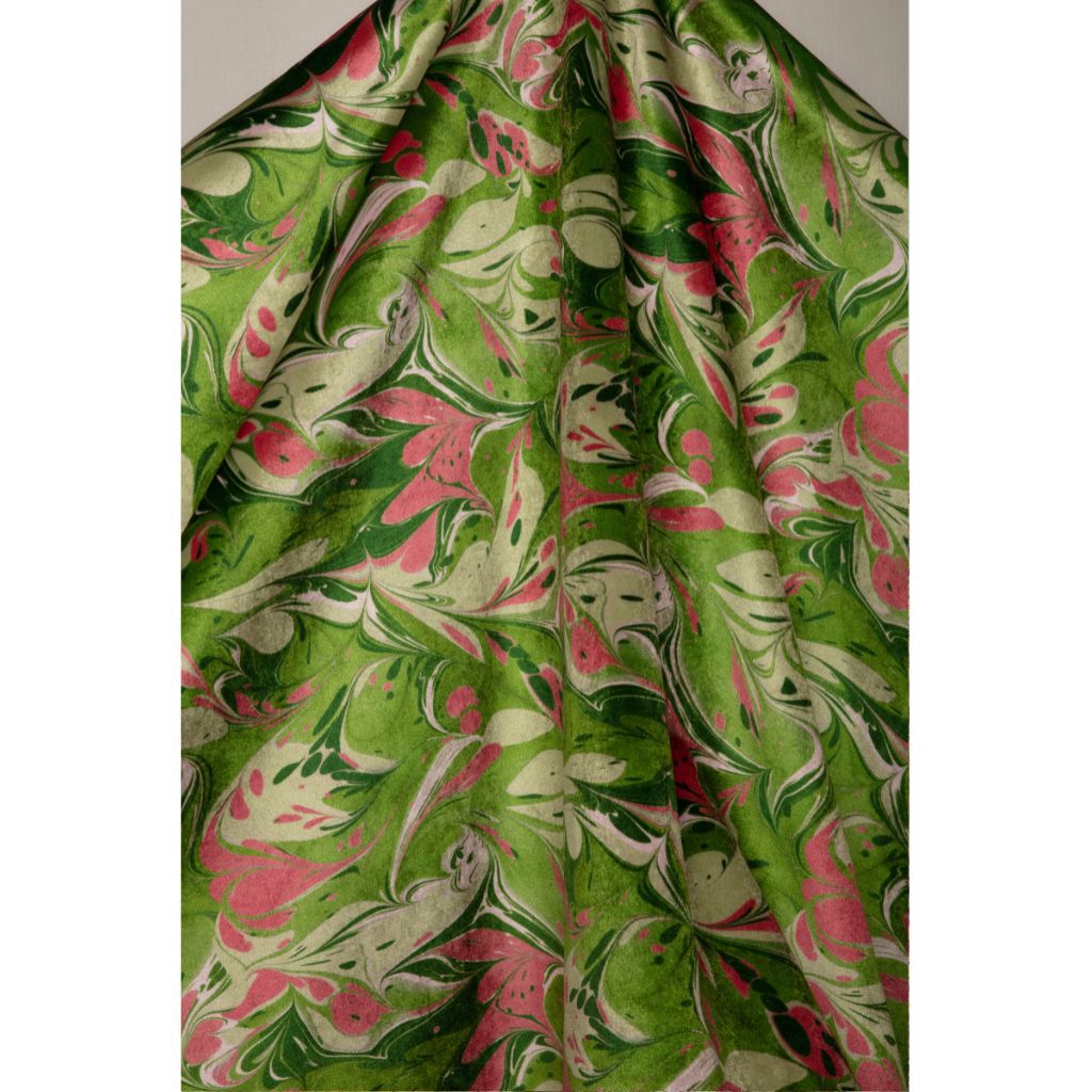 A draped piece of fabric featuring a vibrant green and pink marbled pattern with cream swirls, shown against a neutral gray background.