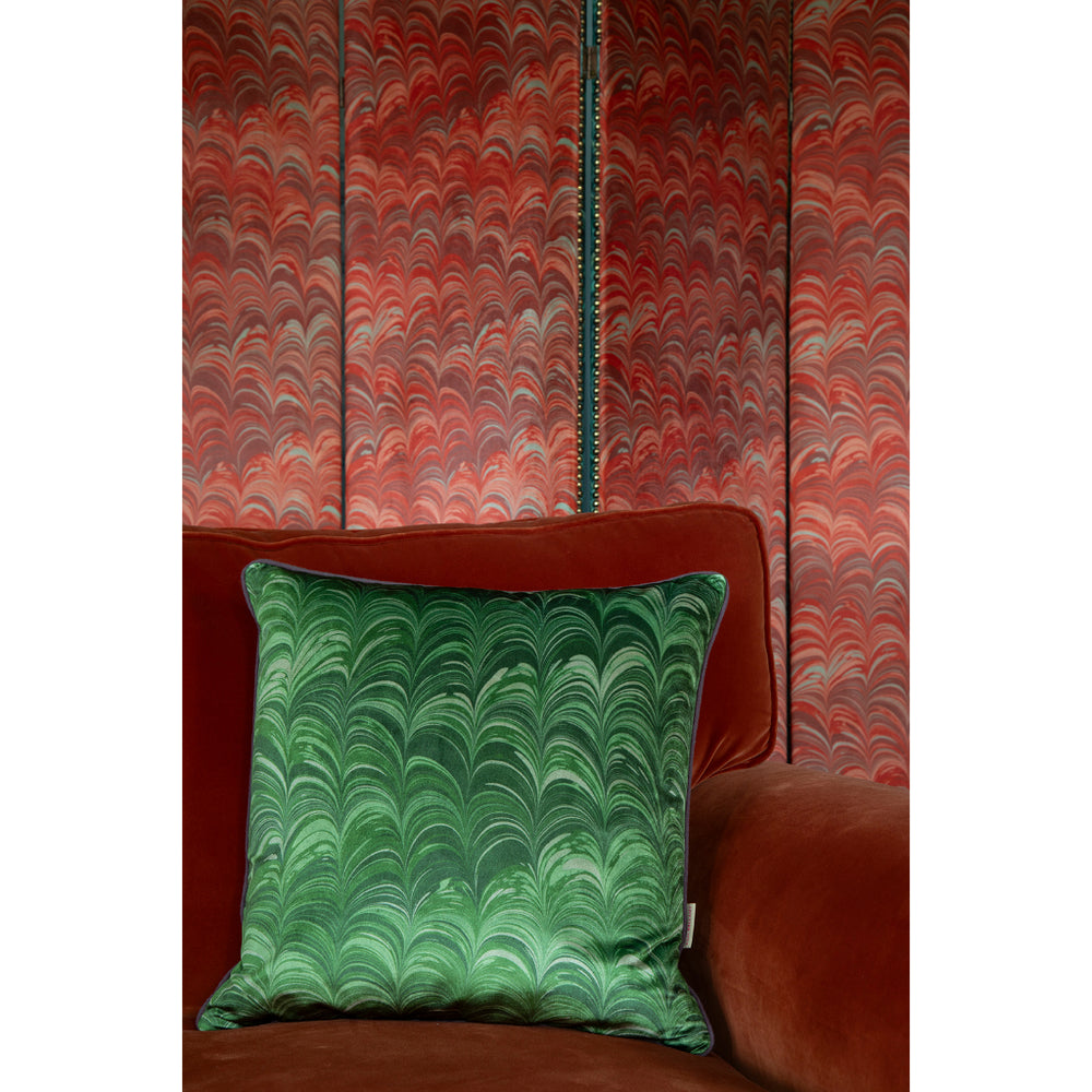 Green marbled pillow on a orange velvet sofa against a red and orange patterned wall.