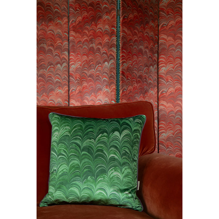 Green marbled pillow on a orange velvet sofa against a red and orange patterned wall.