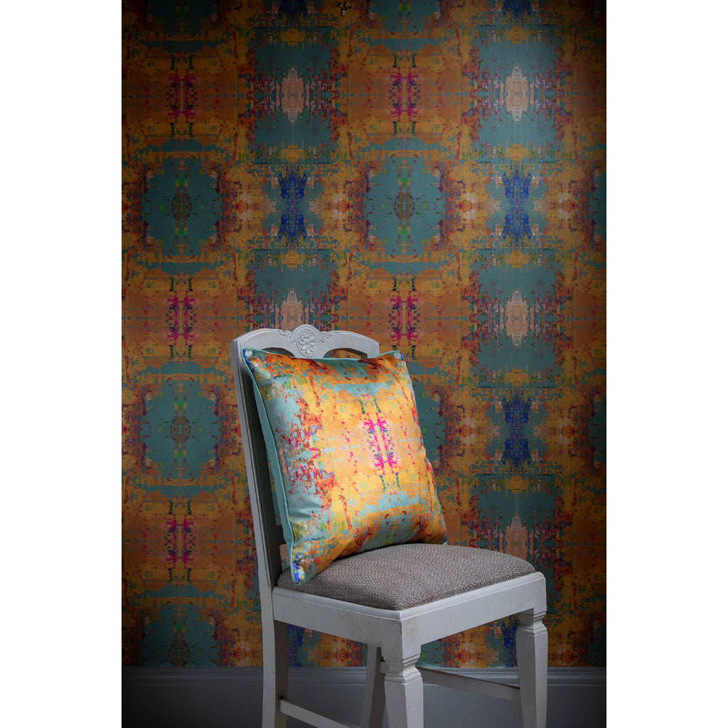 Chair with a colourful abstract velvet pillow against a patterned wall.