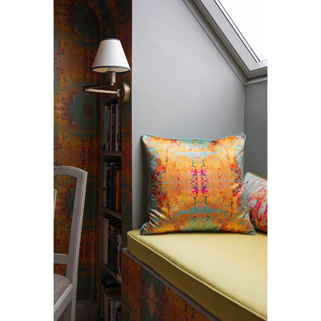 Colourful abstract pillow on a window seat with a bookshelf and lamp in the background