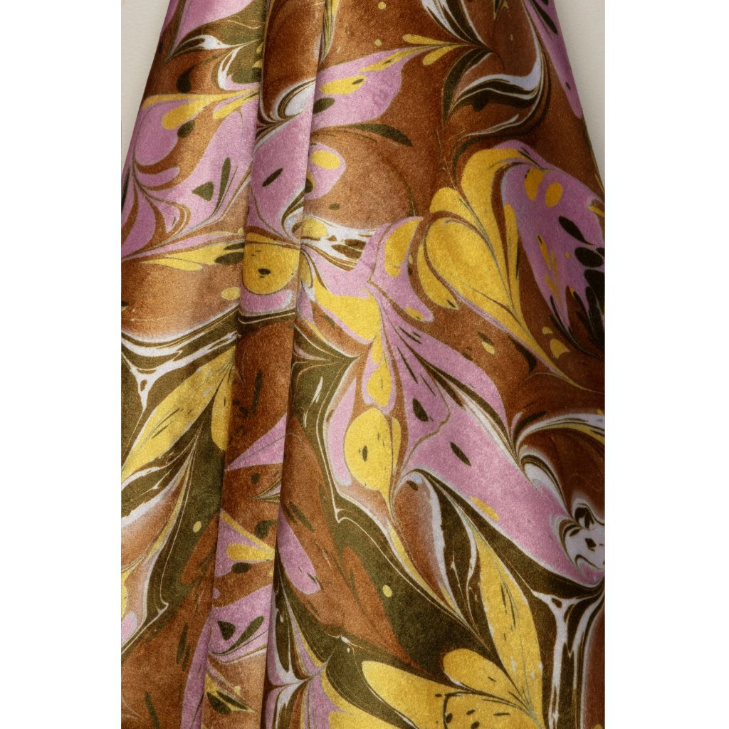 A close-up of a draped fabric with an abstract marbled pattern in brown, yellow, pink, olive green, and white.