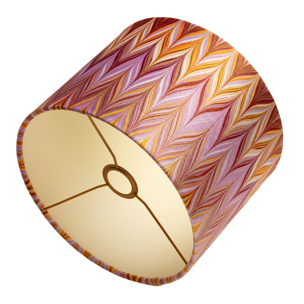 A cylindrical lampshade with a vibrant chevron pattern in shades of pink, orange, red, and yellow, featuring a warm coloured interior.