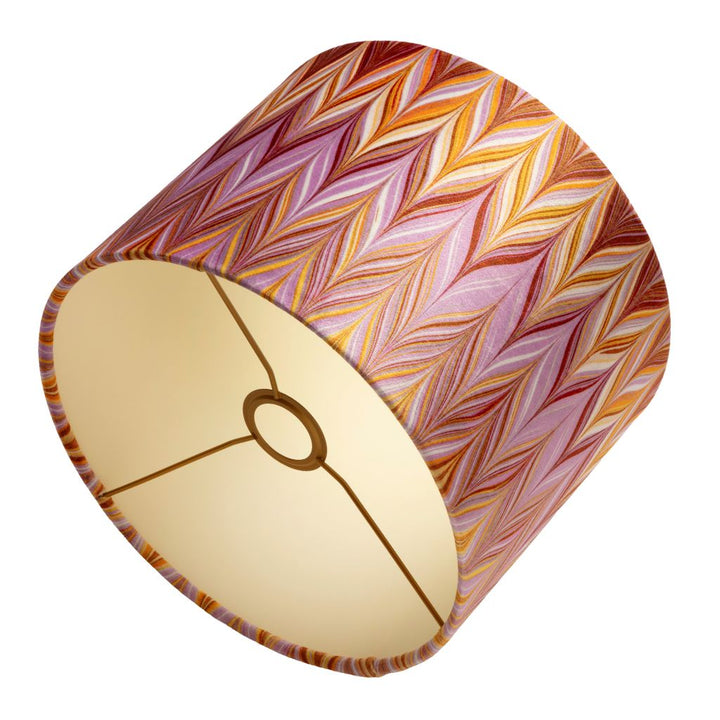 A cylindrical lampshade with a vibrant chevron pattern in shades of pink, orange, red, and yellow, featuring a warm coloured interior.