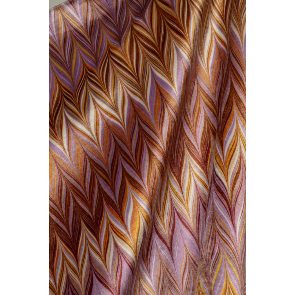 A close-up of a draped fabric with a textured chevron pattern in warm brown, gold, orange, and lavender-purple tones.