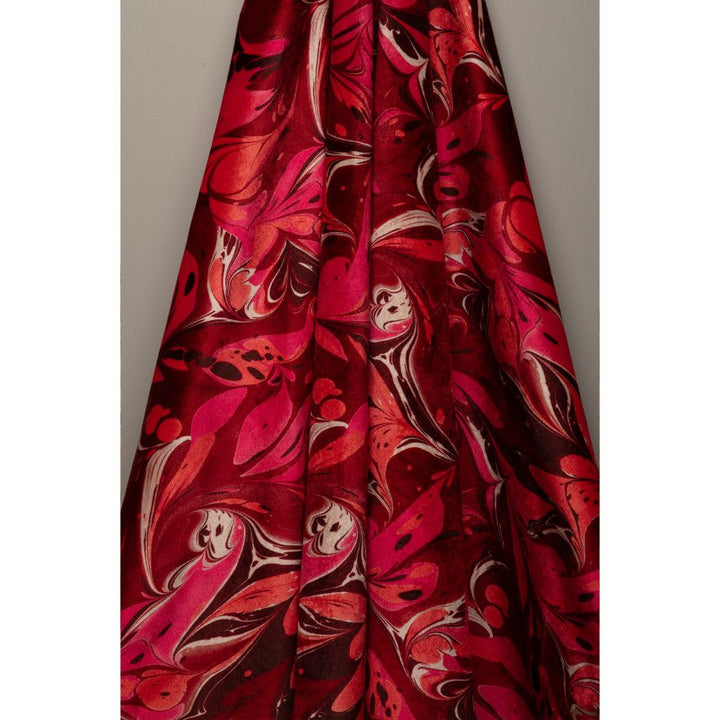 A close-up of a draped fabric with a bold abstract marbled pattern in vibrant red, magenta pink, and dark brown, set against a plain gray background.