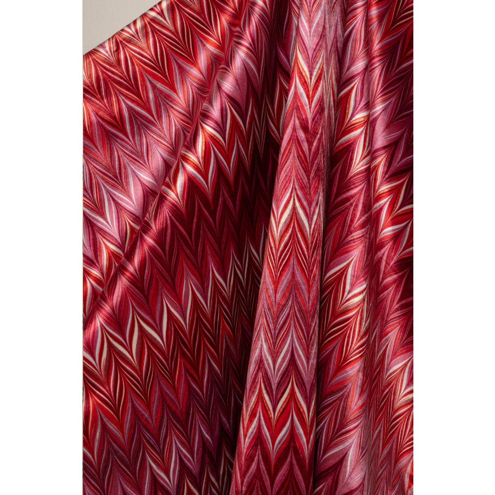 A close-up of draped fabric with a bold zigzag chevron pattern in red, burgundy, pink, and white