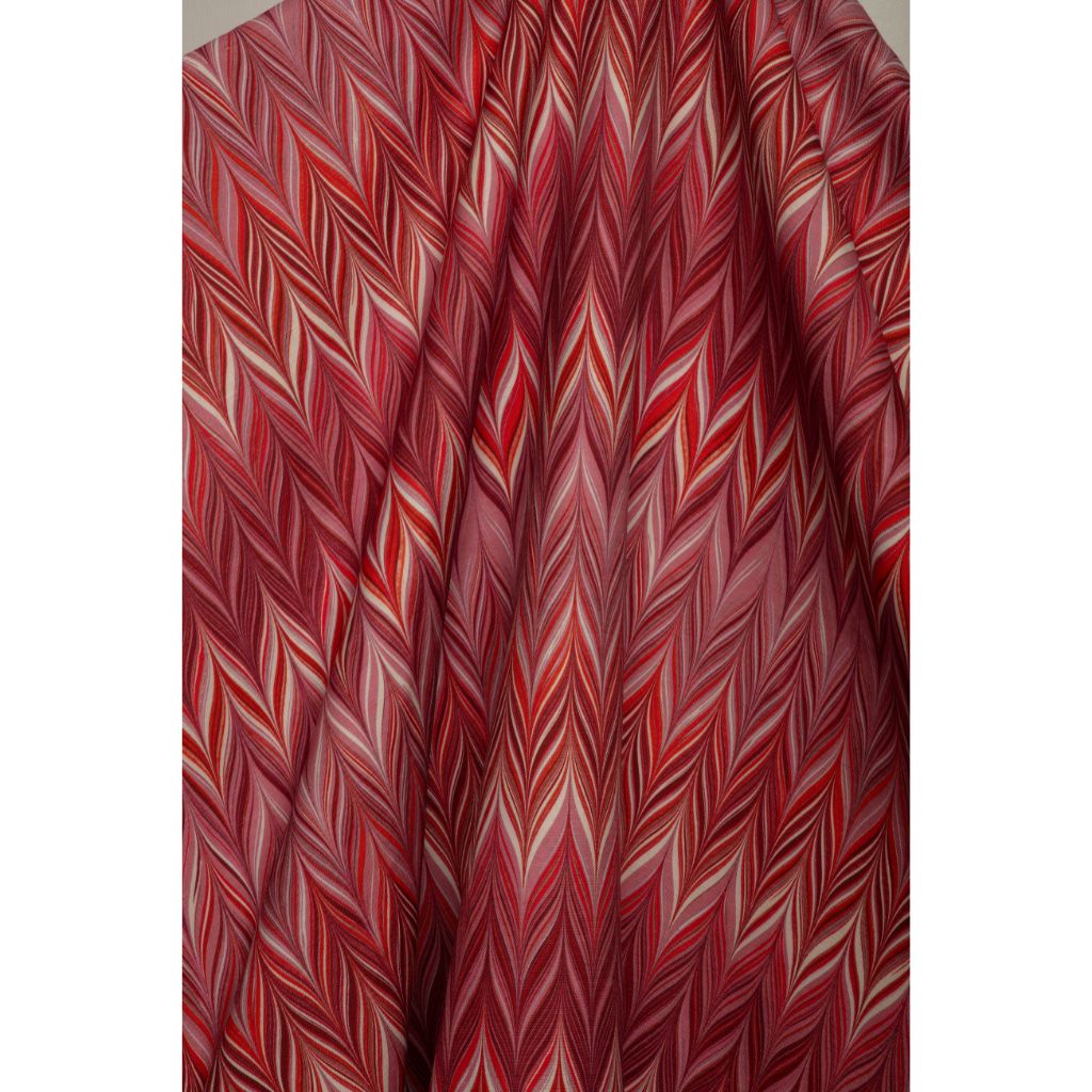 A close-up of draped fabric with a dense, multi-toned chevron pattern in shades of red, pink, and cream.