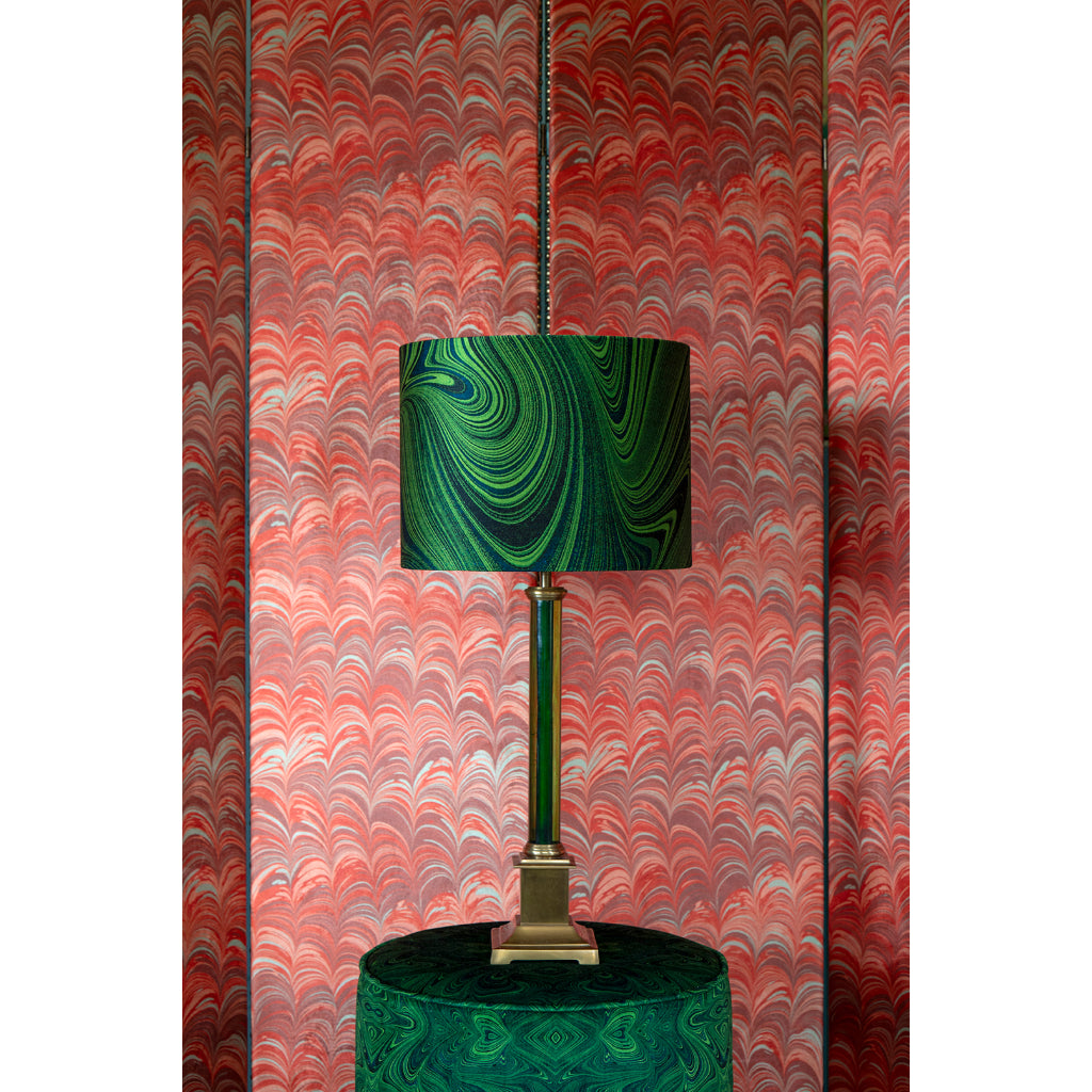 Decorative lamp with a green and gold base against a patterned red and orange upholstered screen
