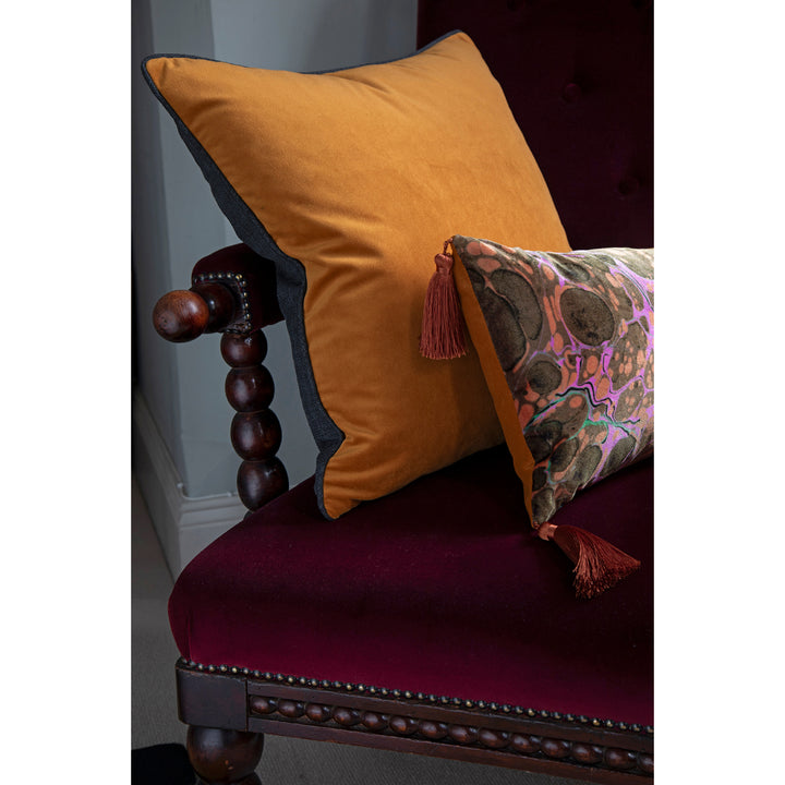 Orange pillow and brown pillow with tassels on a burgundy upholstered chair