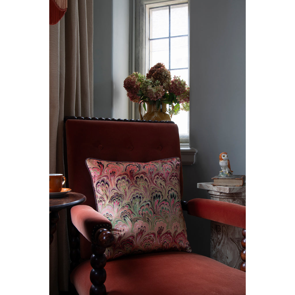 Orange velvet armchair with a marbled pattern pillow in a room with a window and vase with hydrangeas 