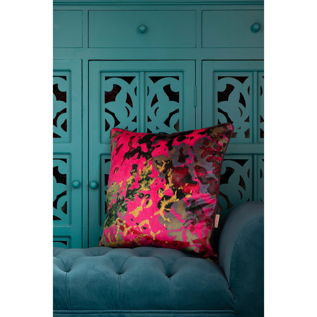 Bright pink pillow on a blue sofa with a teal cabinet in the background