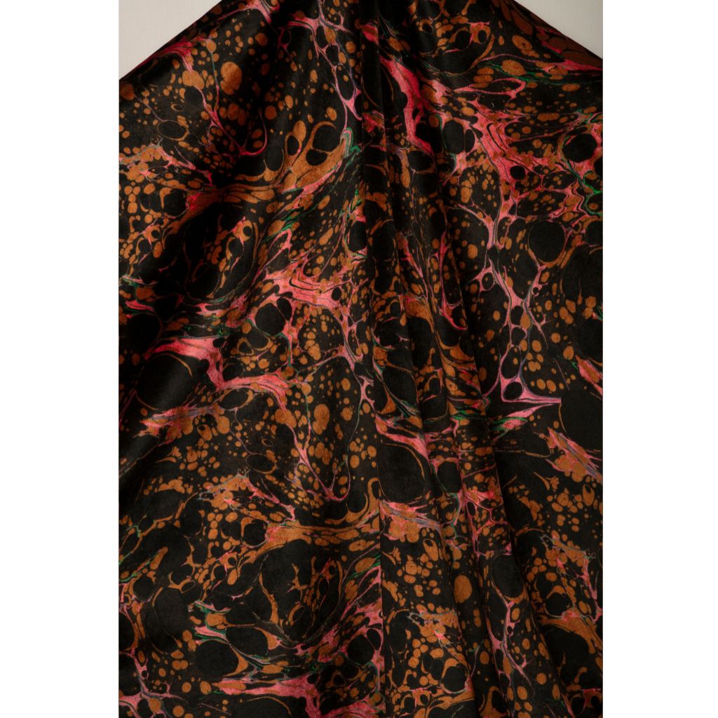 A close-up of a marbled fabric with a black base and abstract splatter pattern in orange, pink, and brown, draped to show its texture and pattern.