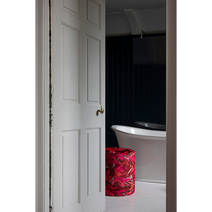 A white panelled interior door is open, revealing a modern bathroom with a white freestanding bathtub and a cylindrical red and pink patterned stool.