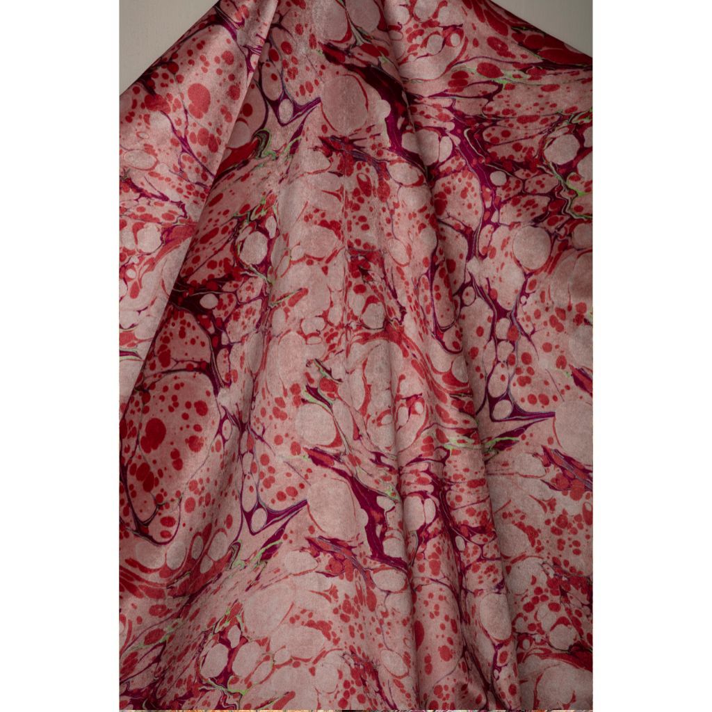 A draped piece of fabric featuring an abstract marbled pattern in shades of red, magenta, and pink over a light bubblegum pink base.