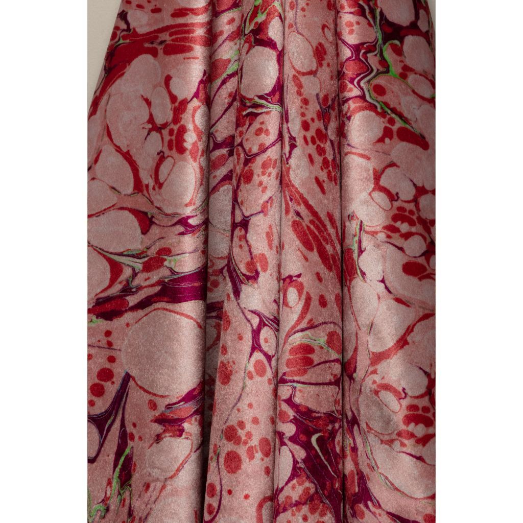 A close-up of draped fabric with an abstract marbled pattern in dusty pink, red, and deep magenta, with small lime green accents.