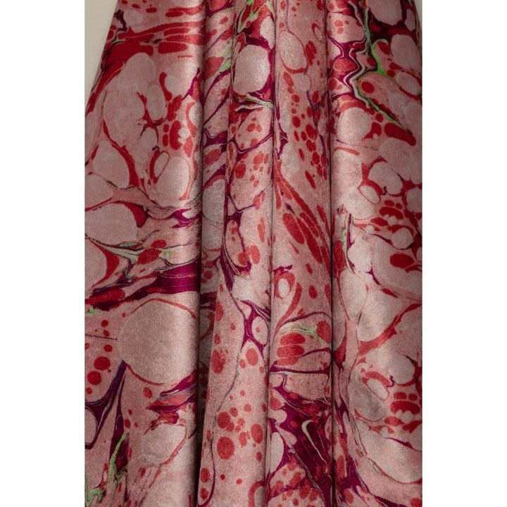 A close-up of draped fabric with an abstract marbled pattern in dusty pink, red, and deep magenta, with small lime green accents.