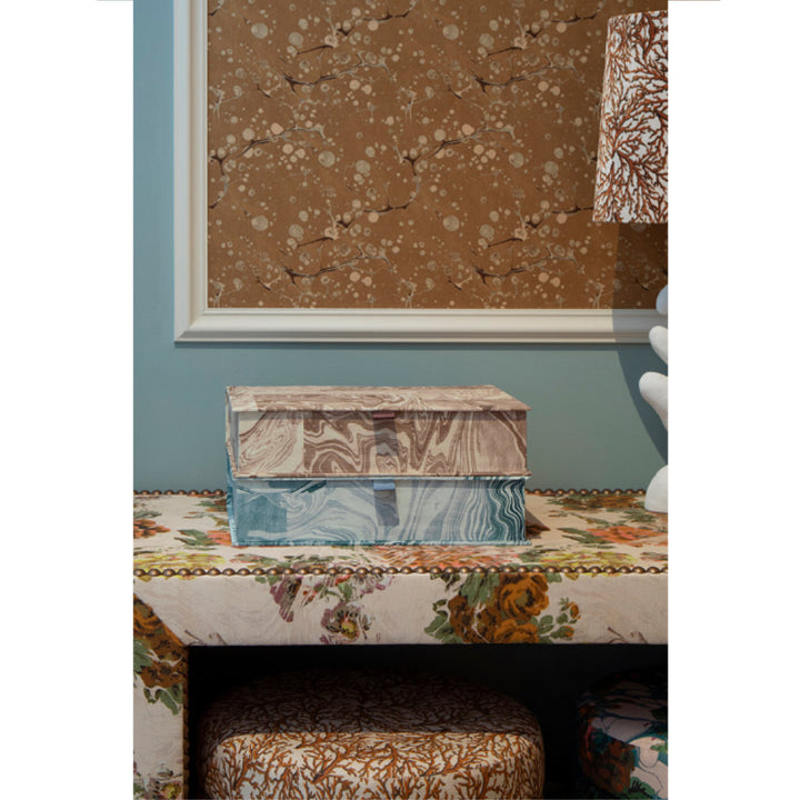 Decorative boxes on a floral-patterned surface with a framed brown and white abstract painting in the background.