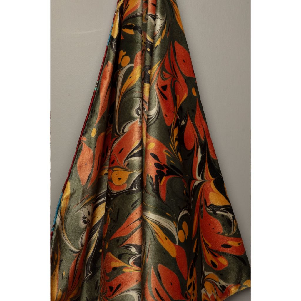 A draped piece of silk fabric featuring an abstract marbled pattern in orange, yellow, black, and gray, shown against a neutral gray background.