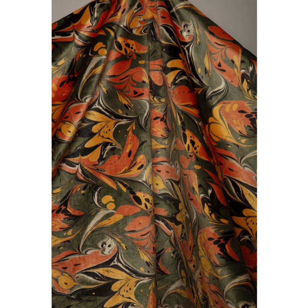 A close-up of a draped fabric with an intricate marbled pattern in olive green, rust orange, mustard yellow, and black.