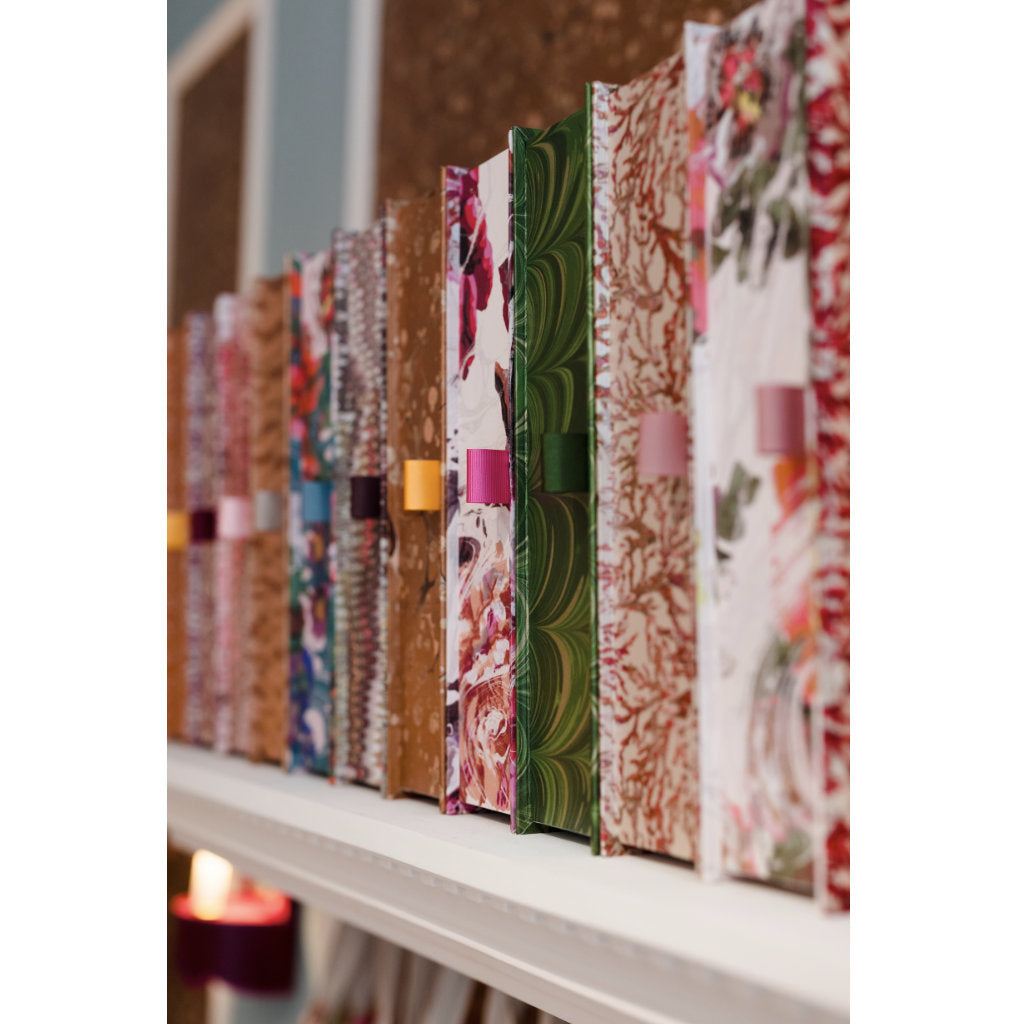 Row of colourful patterned box files on a shelf with a candle in the background