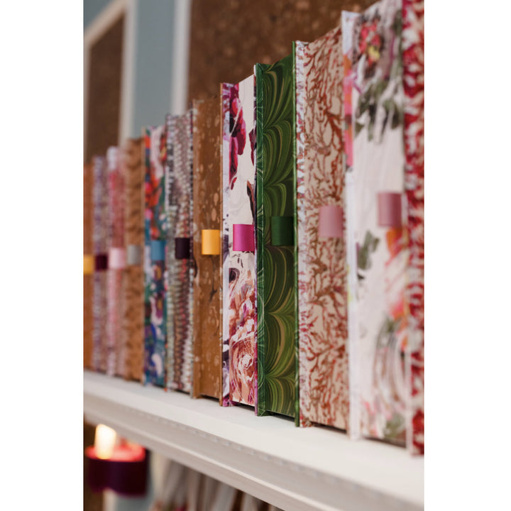 Row of colourful patterned box files on a shelf with a candle in the background