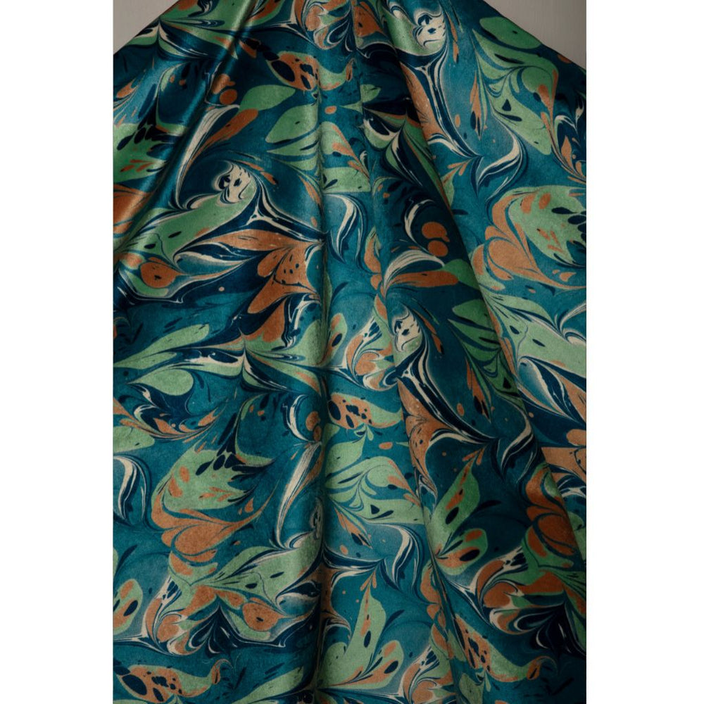 A close-up of draped fabric with an abstract marbled pattern in teal, green, orange, and cream, shown against a light neutral background.