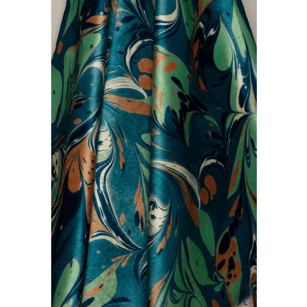 A close-up of draped fabric with an abstract marbled pattern in teal, green, orange, cream, and black.
