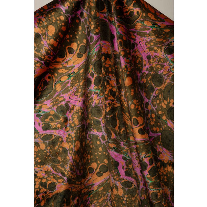 A close-up of draped fabric with an abstract marbled pattern in dark olive green, burnt orange, and bright pink, with scattered black spots.