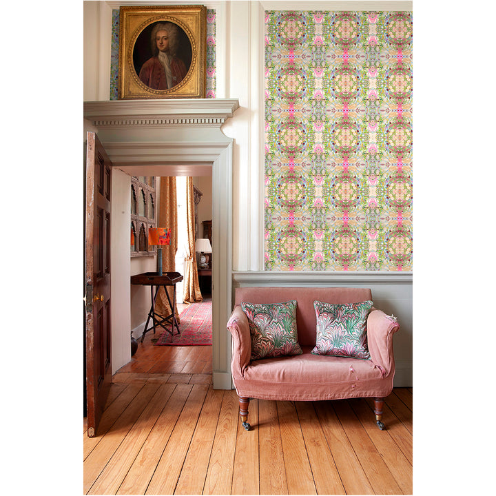 A room with beige ripple wallpaper featuring intricate designs in green, pink, and blue shades. The room includes a pink sofa and matching cushions, a wooden floor, and a painting on the wall.
