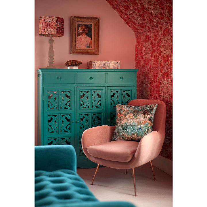 Duck egg blue cushion on pink velvet chair with turquoise cupboard and orange and pink wall and sloped ceiling